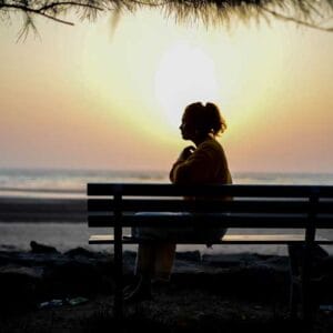 Making Sense of Menopause A woman sits on a bench at sunset.